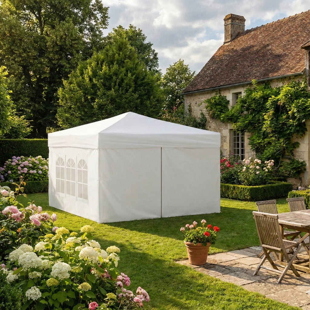 Tente pop-up blanche fermée installée dans un jardin verdoyant à côté d'une terrasse en pierre.
