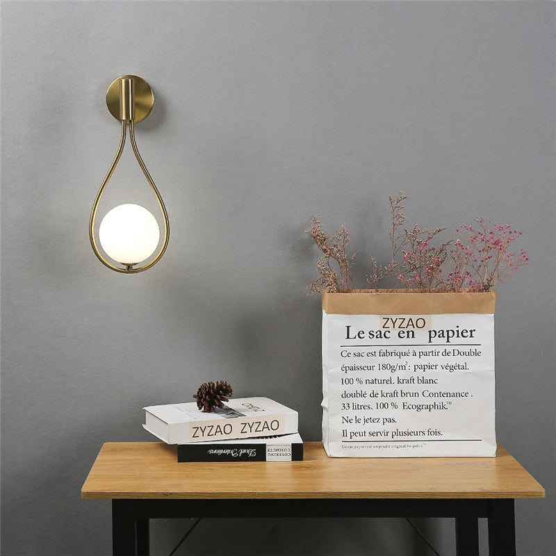 Applique murale dorée avec globe opalin rond, éteinte sur fond neutre – design-elegant