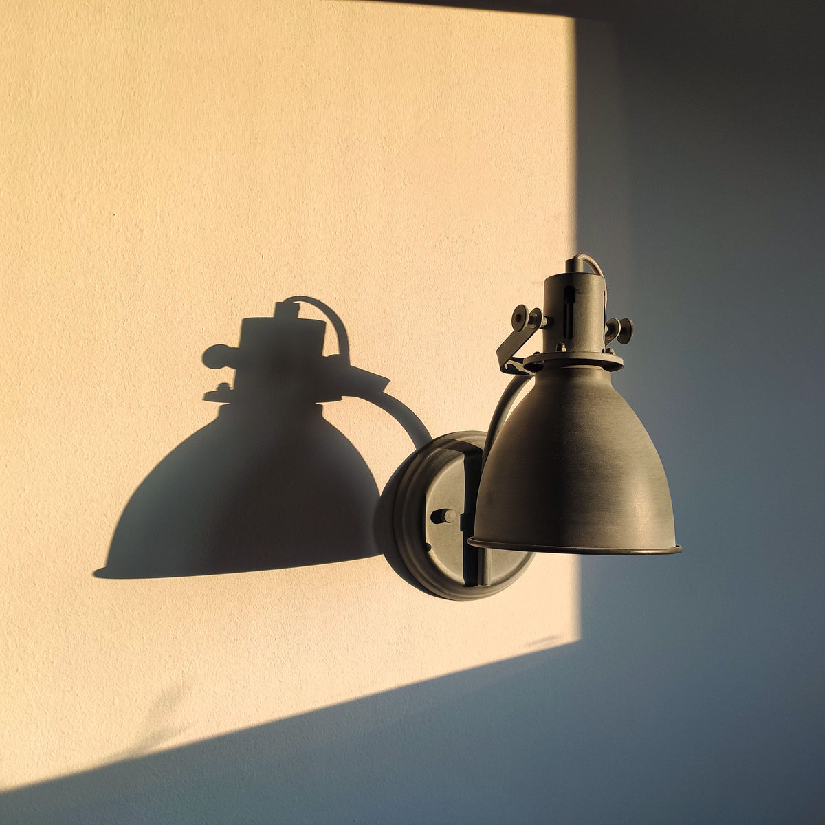 Applique murale industrielle en métal patiné à abat-jour orientable, sur un mur clair éclairé au soleil Image